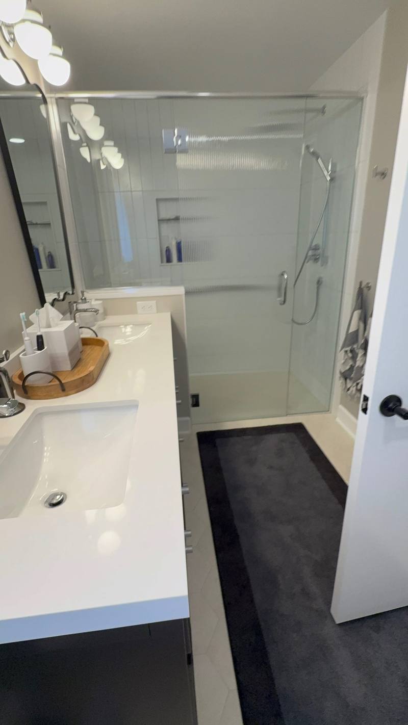 Bathroom remodel with white vanity, dark cabinets and a glass walk-in shower