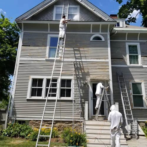 Crew on ladders prepping and painting an older home exterior